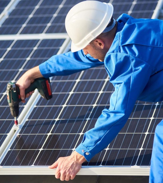 Elektryk montujący panel słoneczny na dachu nowoczesnego domu.